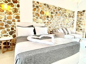 A bedroom with a stone wall, a bed with grey bedding, a sofa, and a small table.