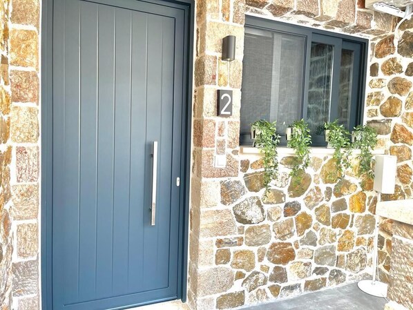 A stone facade with a dark blue door and a window with plants.