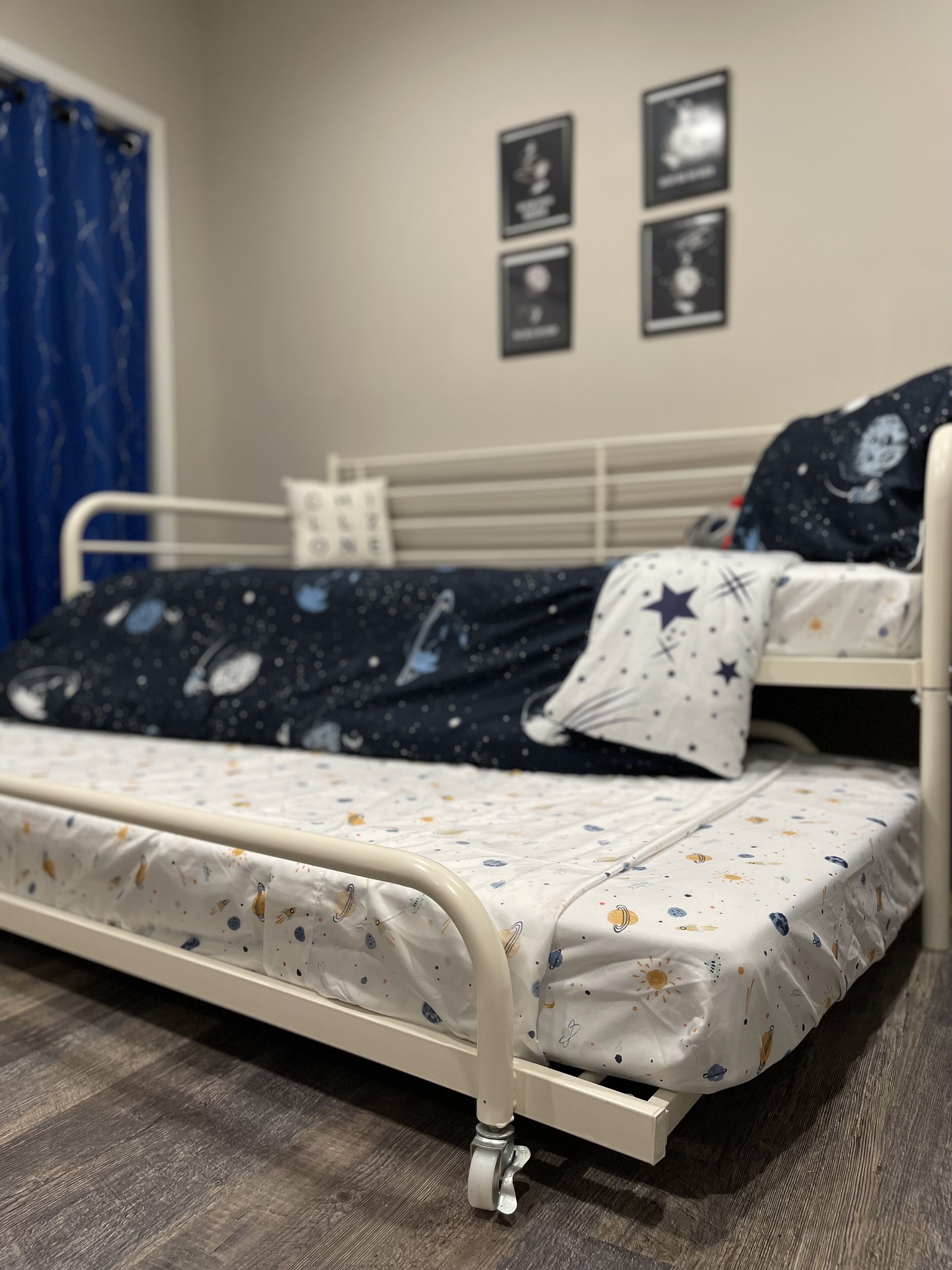 Een enkel bed met een bedovertrek met ruimteprint, een metalen frame en een houten vloer.