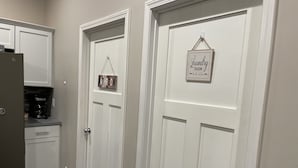 A kitchen with a refrigerator, coffee maker, and pet bowls. There are two white doors, one labeled "Bathroom" and the other "Laundry Room".