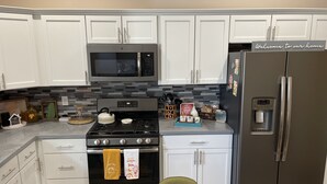 A modern kitchen with white cabinets, a stainless steel refrigerator, a microwave, and a stove.