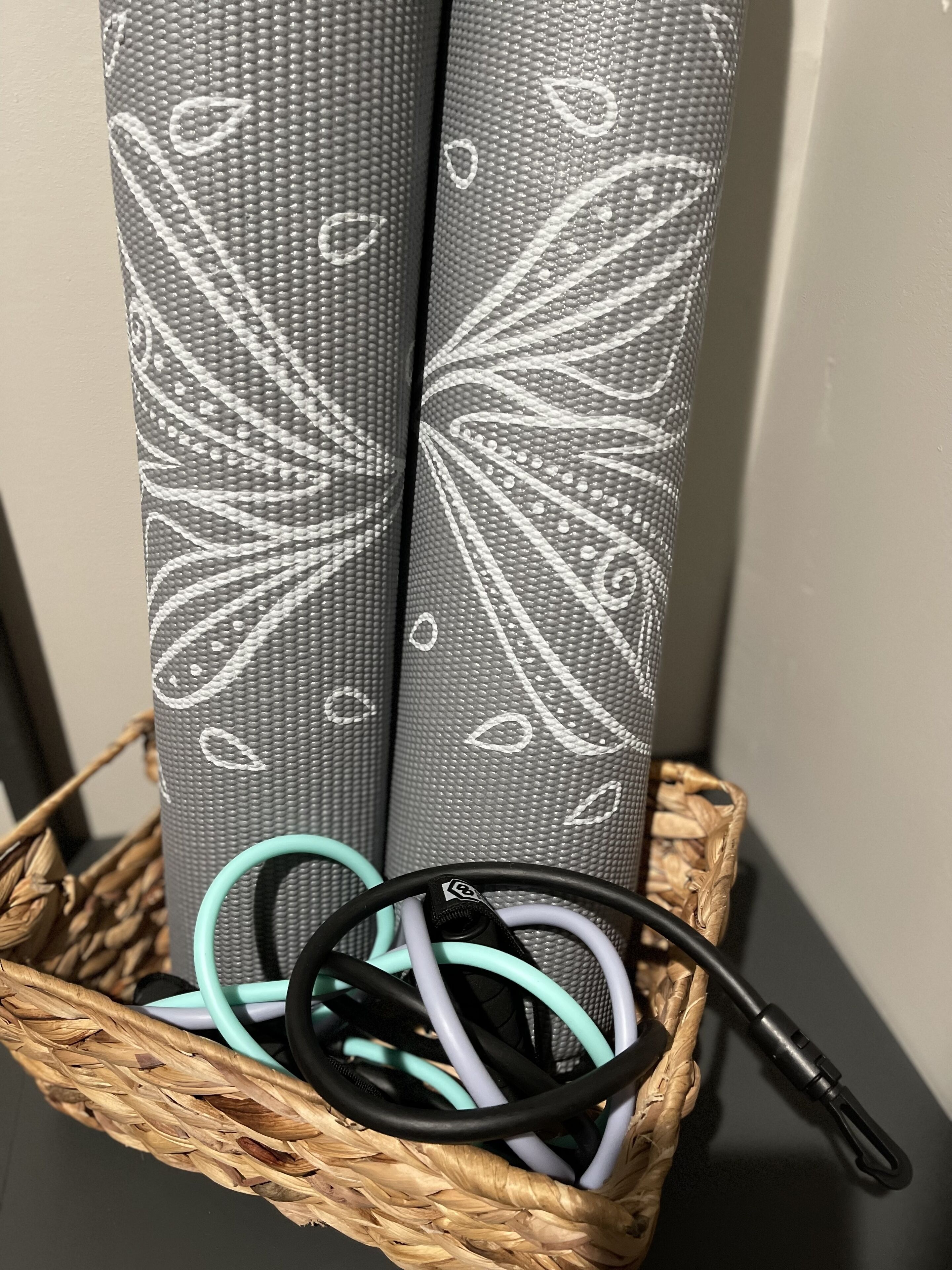 Two yoga mats with white designs in a woven basket.