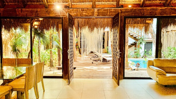 Ein tropisches Resort-Interieur mit einem Reetdach, Holzboden und einem Poolbereich, der durch den offenen Raum sichtbar ist.