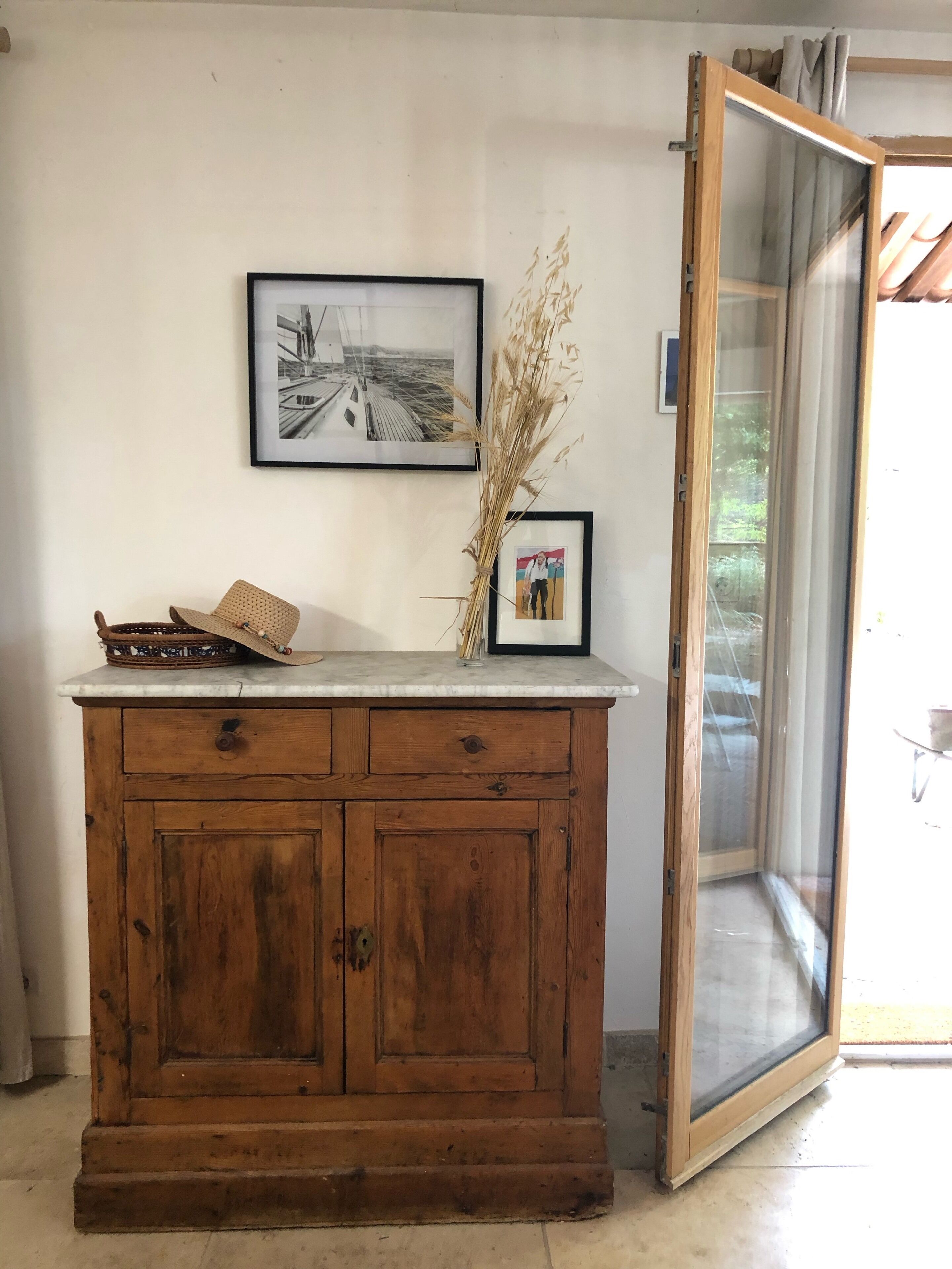 A wooden cabinet with a marble top, a framed black and white photo, and a vase with dried plants.