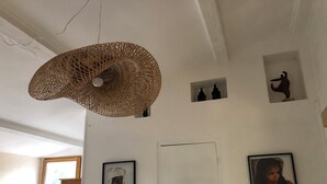 Habitació amb un llum de sostre teixit, una porta i dues fotografies emmarcades a la paret.