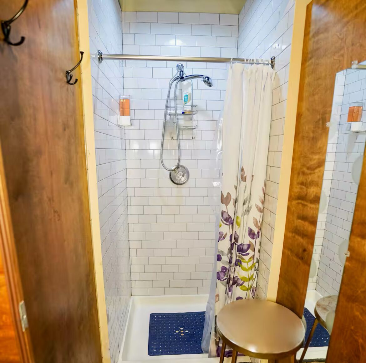 A small, enclosed shower area with a showerhead, a toilet, and a small stool.