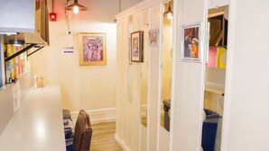 A narrow hallway with a white partition, wooden flooring, and a dining area with a table and chairs.