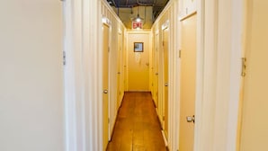 A narrow hallway with doors on both sides, a wooden floor, and an exit sign above.