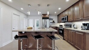A modern kitchen with a central island, bar stools, stainless steel appliances, and wooden cabinets.