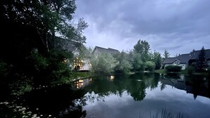 Ein friedlicher Seeblick mit einem Haus, das sich im Wasser spiegelt, umgeben von Bäumen und einem Steg.