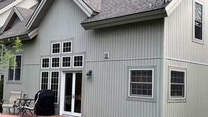 Ein zweistöckiges Haus mit einer überdachten Terrasse, einer Schiebetür und einer kleinen Sitzgelegenheit mit Stühlen.