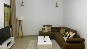A living room with a sectional sofa, a flat-screen TV on a stand, a coffee table, a lamp, and an air conditioning unit. - Villa within walking distance to the beach!!! (Saly)