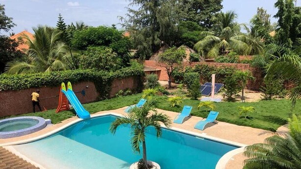 A swimming pool with a slide, lounge chairs, and a palm tree. - Villa within walking distance to the beach!!! (Saly)
