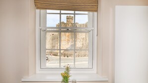 A dining table set with white plates, bowls, and cutlery, a vase with flowers, and a wine glass. A window with a view of a castle is above the table. - Moel Tryfan (Caernarfon)