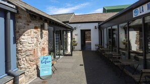 A courtyard with stone walls, a sign for 'Stop Eifion' offering bespoke gifts and homeware, and a 'LA Kitchen' sign. - Moel Tryfan (Caernarfon)