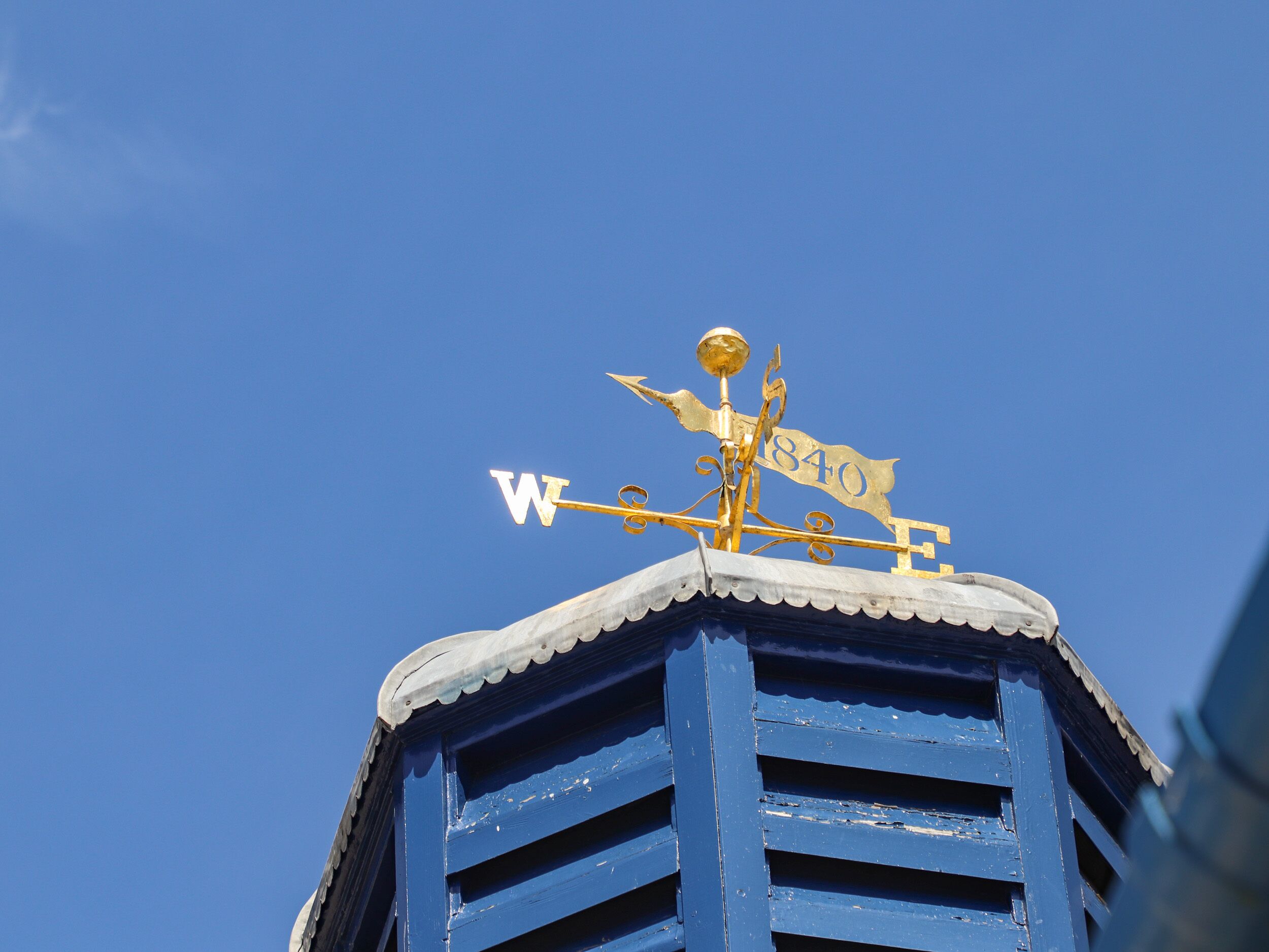 Vaneador de vento com o número 840 e as letras W, E, N, S no telhado de um edifício.