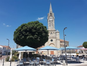 Ein Platz mit Außenbestuhlung, ein großer Baum und eine Kirche mit einem hohen Turm.