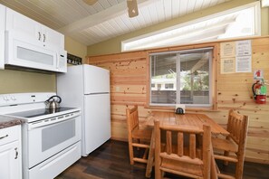 A compact kitchen with white appliances, a wooden table, and a window with blinds.