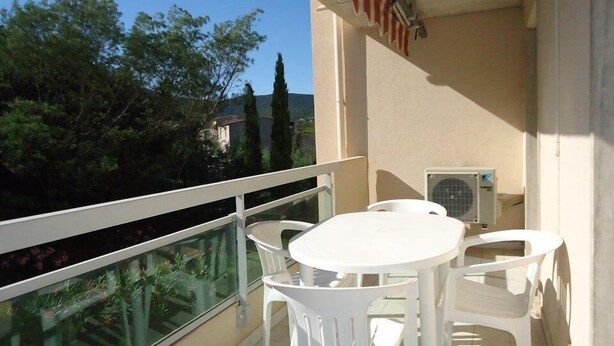 Un balcon doté d’une balustrade en verre, de chaises en plastique blanc et d’une table.