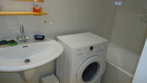 Une petite salle de bain comprenant un lavabo, un lave-linge et un petit meuble de rangement.