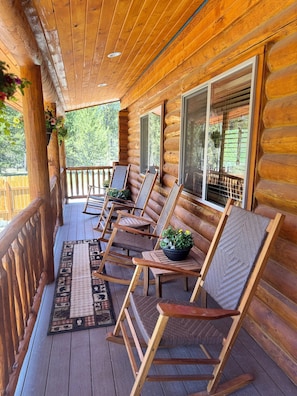 A wooden log cabin with a porch featuring rocking chairs and a potted plant.