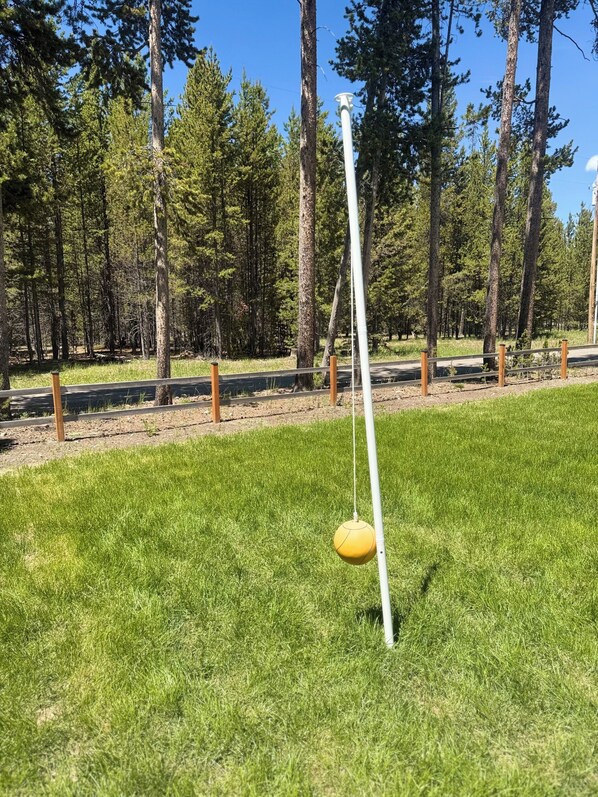 A grassy area with a yellow ball on a white pole, surrounded by trees and a fence.