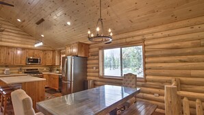 Una cocina de cabaña de troncos con armarios de madera, un refrigerador de acero inoxidable, una isla grande con taburetes y una lámpara de araña.