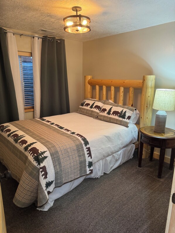 Een slaapkamer met een houten hoofdbord, een bed met een sprei met dierenprint, een bedlampje en een raam met gordijnen.
