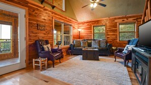 A cozy log cabin interior with a wooden floor, a leather sofa, a fireplace, and a television.