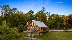 A wooden cabin with a deck, surrounded by trees and grass.