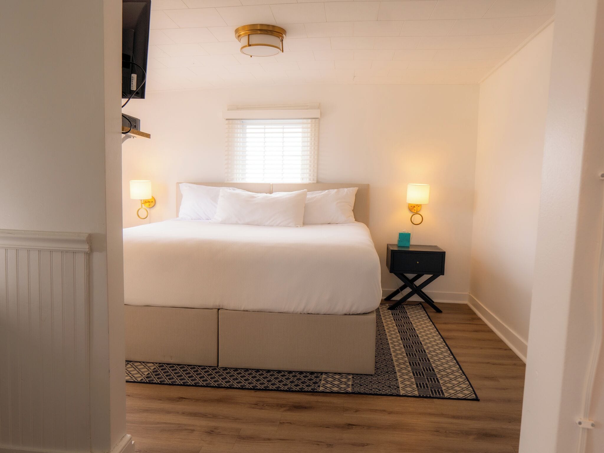 Une chambre à coucher avec un lit, des lampes de chevet, une fenêtre avec des stores et un tapis à motifs.