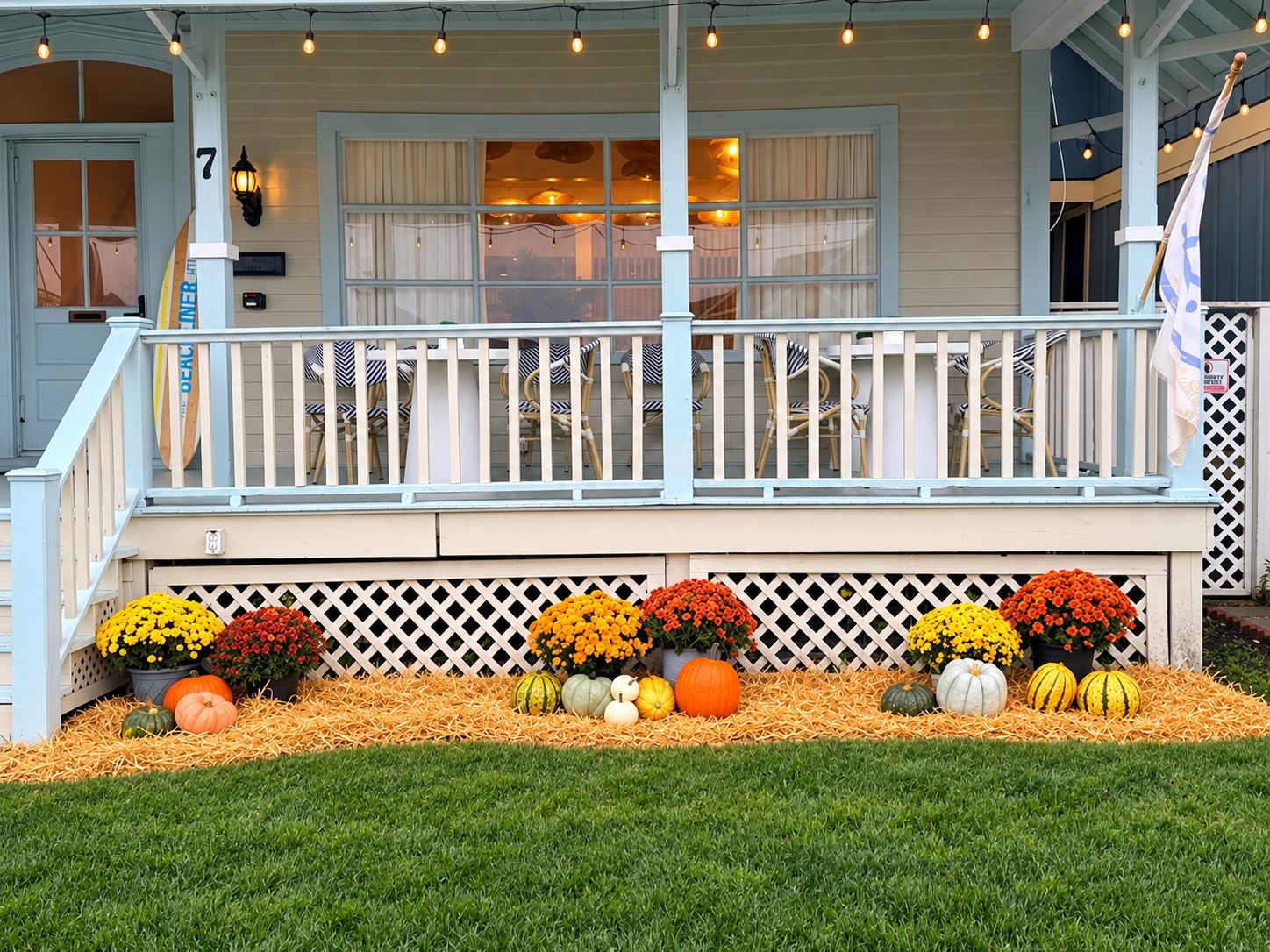 A porch with a white railing, a flag, and a variety of pumpkins and flowers.