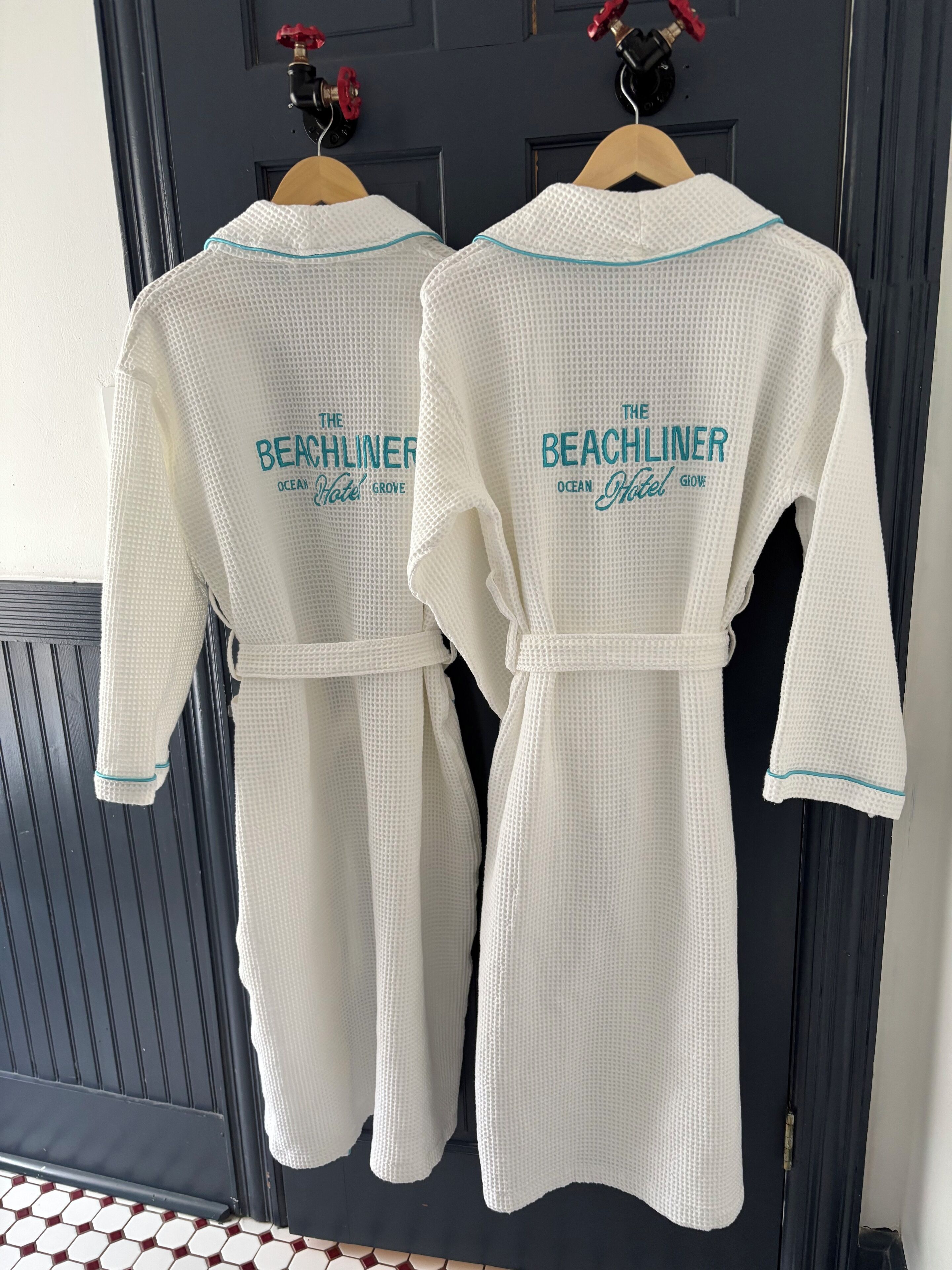 Two white bathrobes with "The Beachliner" text hanging on a door.