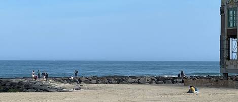 A beach with a rocky breakwater and a building with a lighthouse on top.