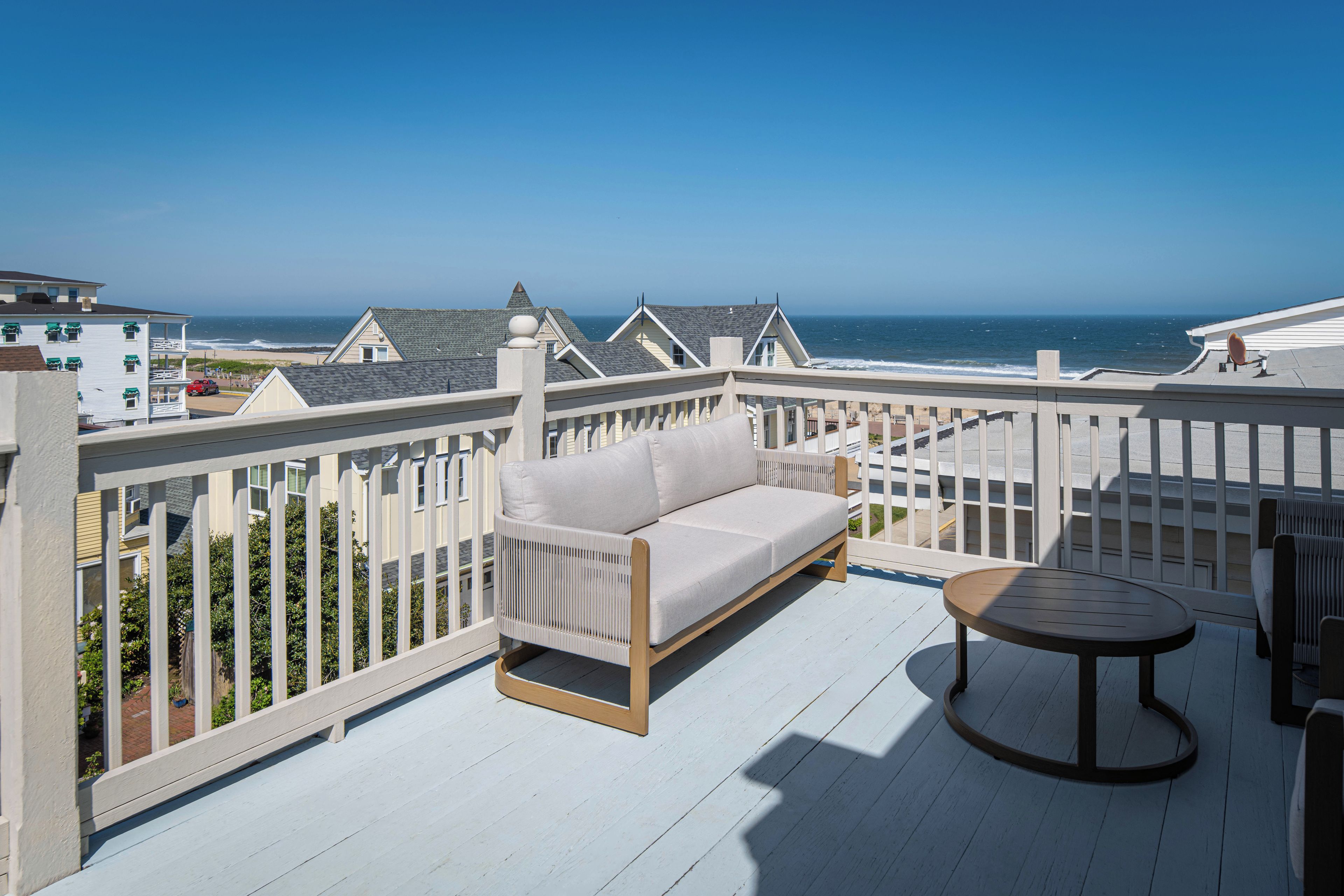 Un balcon avec un canapé blanc et une table ronde, donnant sur une plage et l’océan.