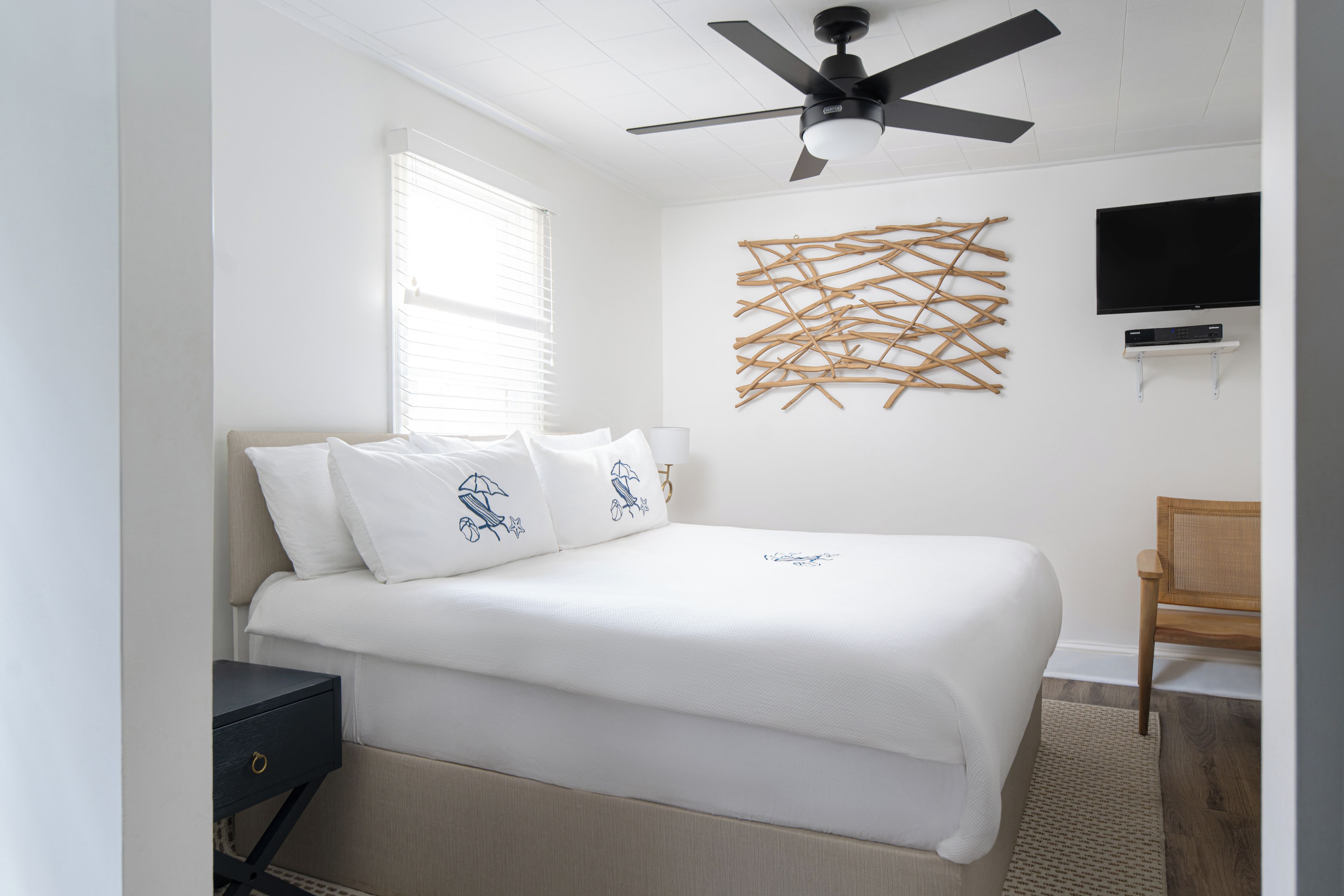 A bedroom with a bed, a ceiling fan, a wall-mounted TV, and a decorative wall piece.