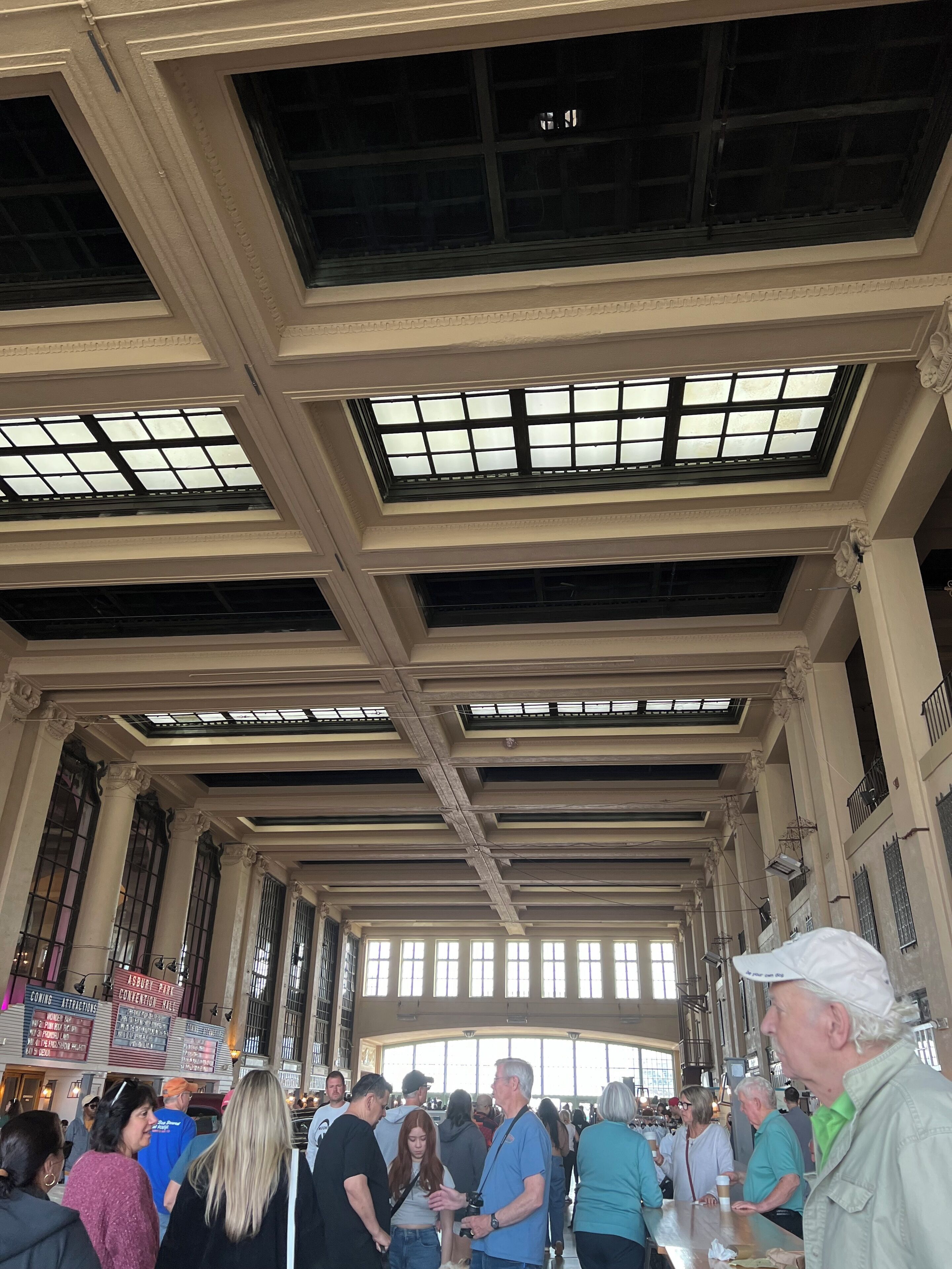 A spacious indoor area with high ceilings and large windows, featuring a central open space with people gathered around.
