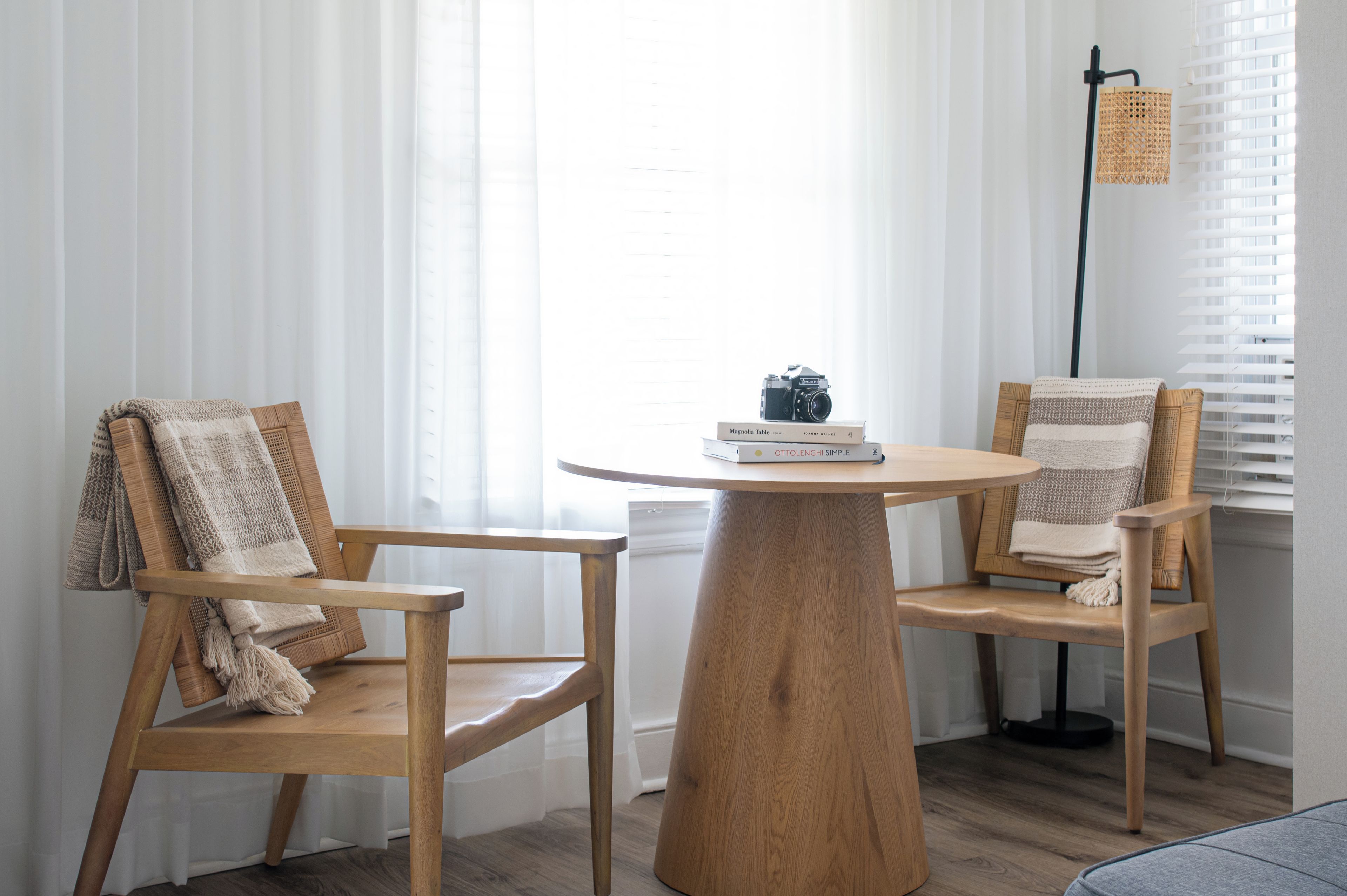 Una habitación con dos sillas de madera, una mesa redonda de madera y una lámpara de pie.