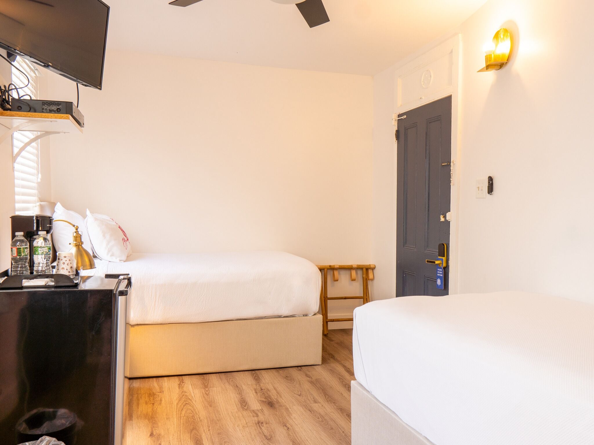 Quarto de hotel com duas camas, uma mesa de trabalho com televisão e chão de madeira.