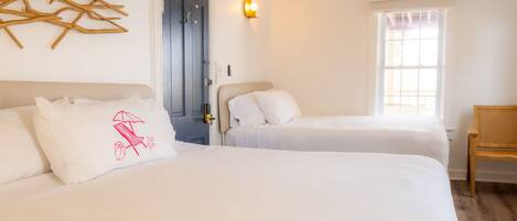 A hotel room with two beds, a wooden chair, a wall-mounted light, and a door with a handle.