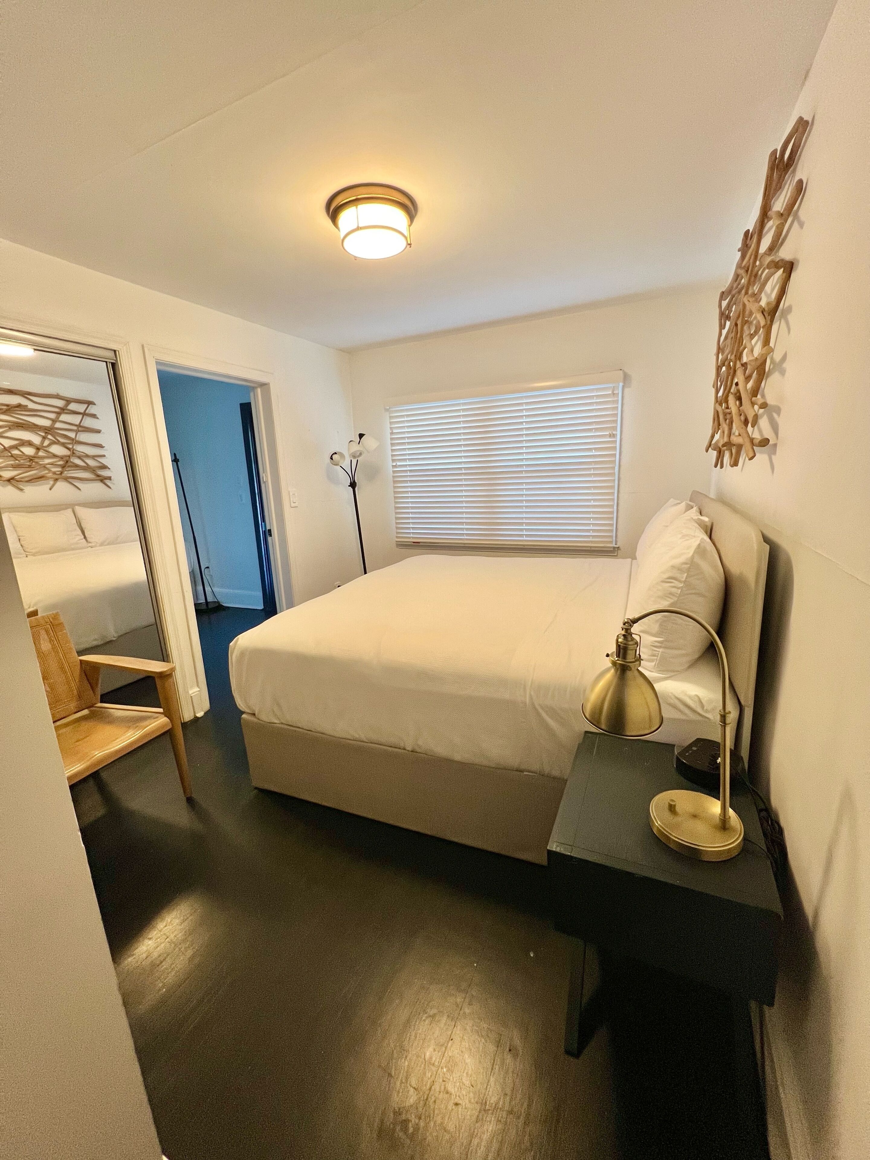 A bedroom with a bed, bedside lamp, and a window with blinds.