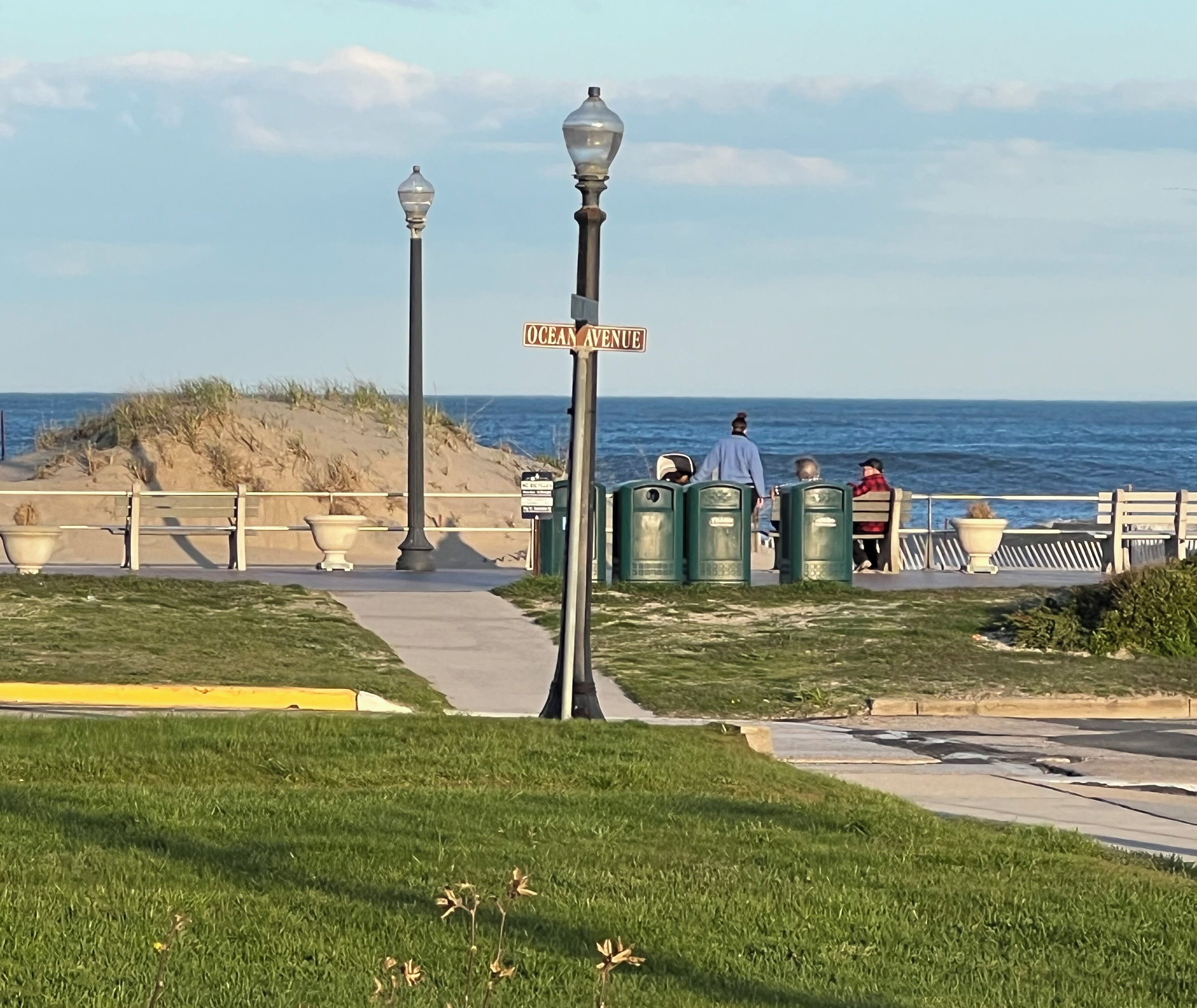A bench-lined walkway with a street sign reading "Ocean Avenue" and a view of the ocean.