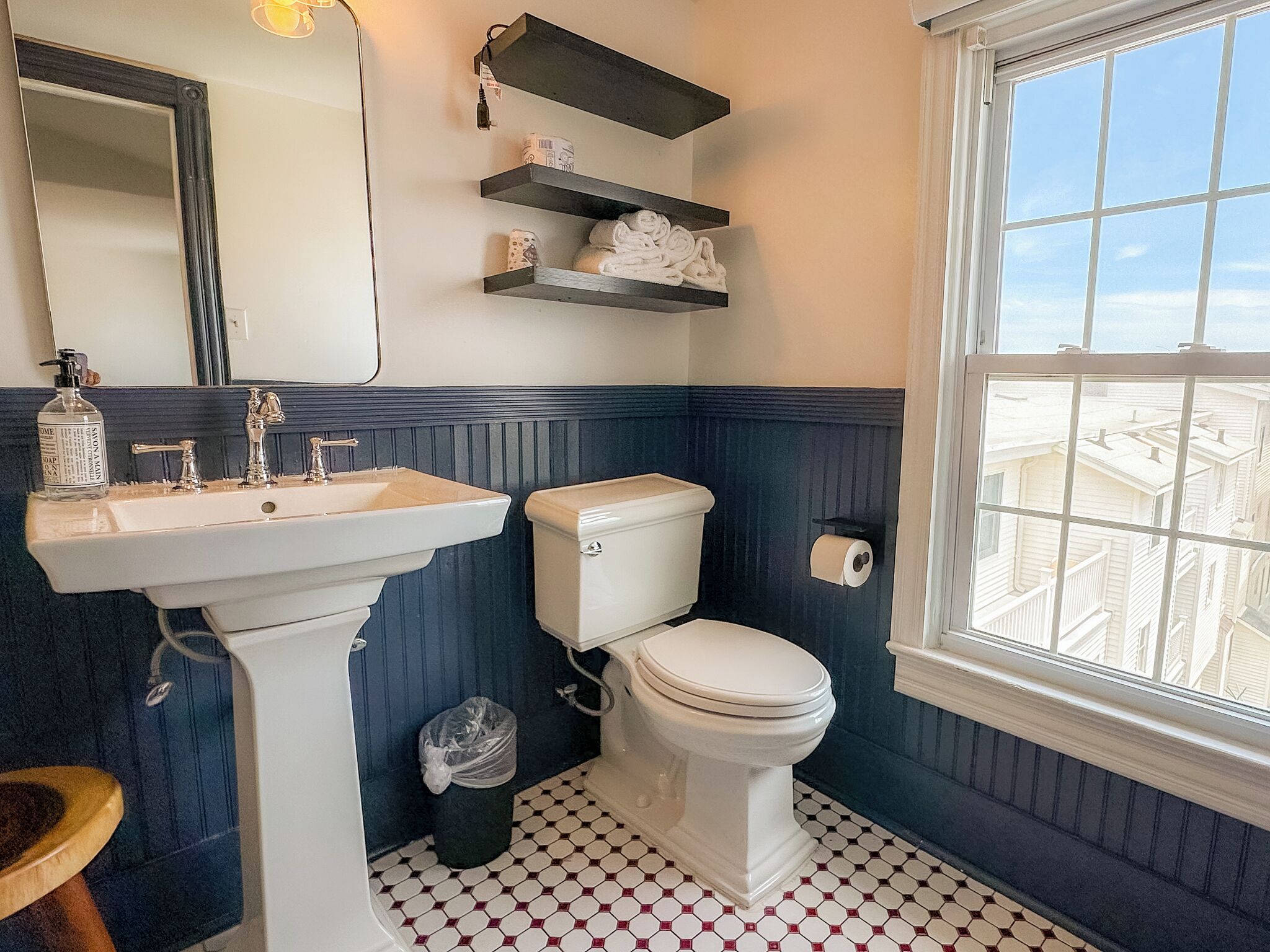 A bathroom with a pedestal sink, toilet, and a window with a view of buildings.