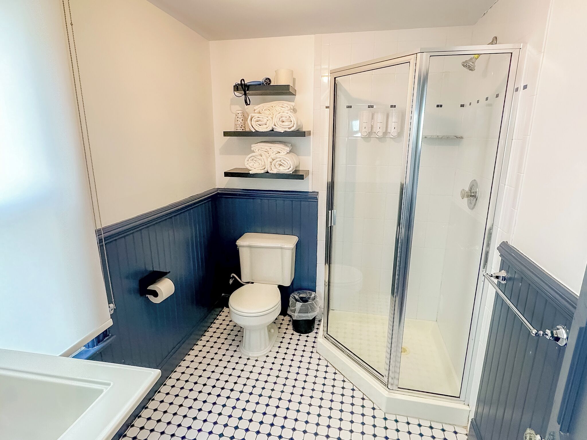 Un baño con inodoro, ducha con puerta de vidrio y repisas con toallas.