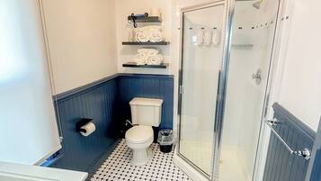 Un baño con inodoro, ducha con puerta de vidrio y repisas con toallas.