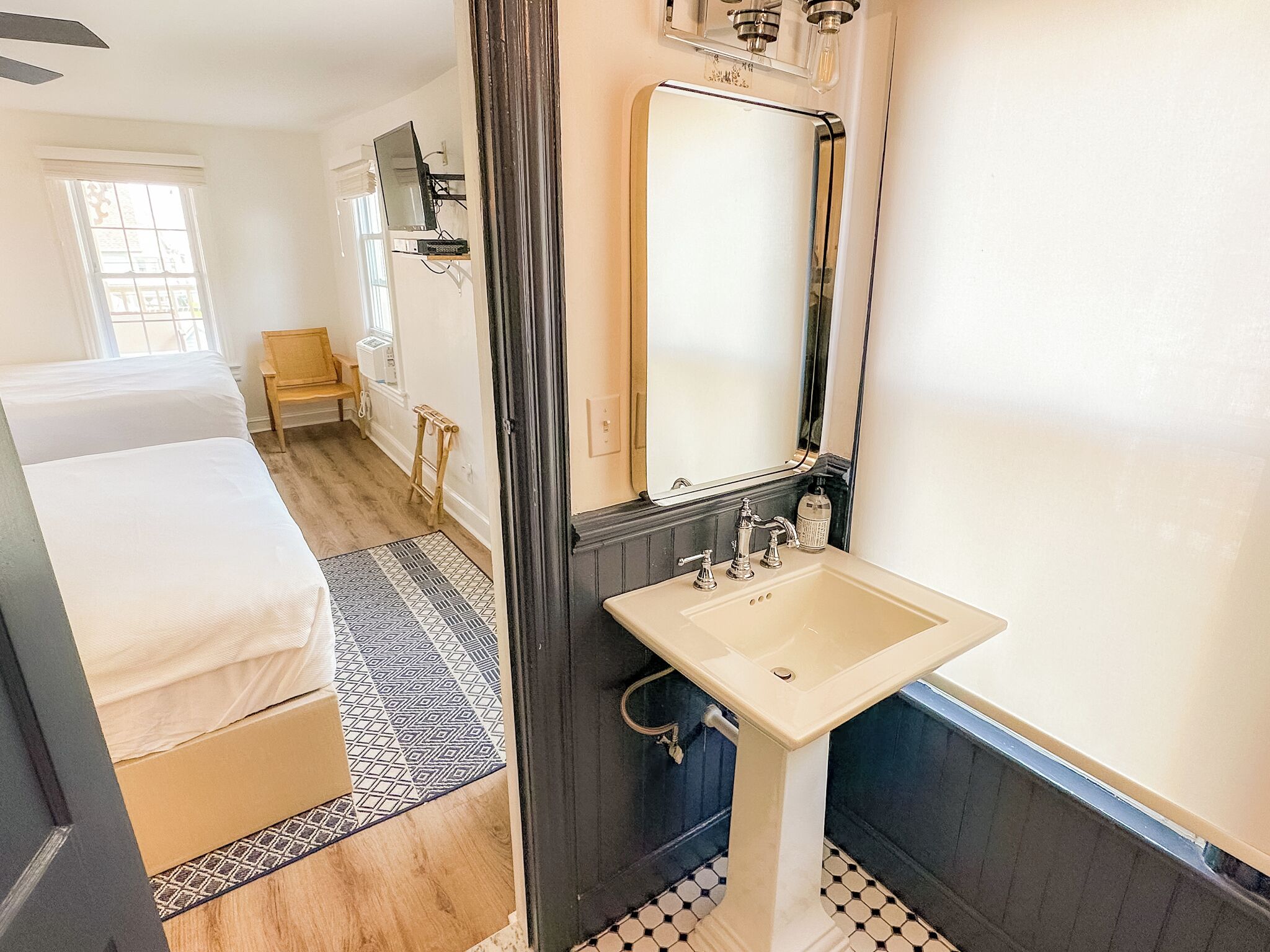 Ein Hotelzimmer mit Bett, Bad mit Waschbecken und Spiegel sowie einem Fenster mit Vorhängen.