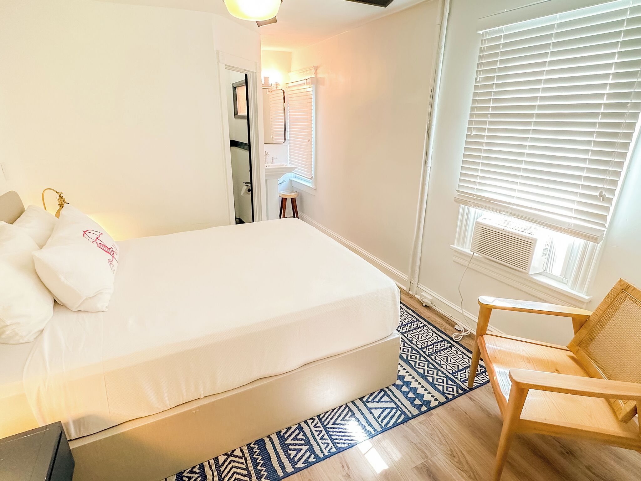 Una camera da letto ordinata con un letto, una sedia, un tappeto decorato e una finestra con persiane.