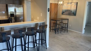 A modern kitchen with stainless steel appliances, a bar area with stools, and a wooden dining table. - BEAUTIFUL & SPACIOUS 2BR/2BA BEACH CONDO (Jacksonville Beach)
