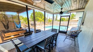 Eine überdachte Terrasse mit Pool, Holzmöbeln und Deckenventilator.