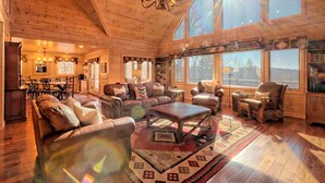 A spacious log cabin interior with a large living area, leather furniture, a chandelier, and large windows offering views of the outdoors. - Sunset Mountain Views- Spacious Luxurious cabin (Morganton)